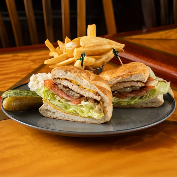 A chicken sandwich with lettuce, tomato, bacon, and cheese, served with fries, coleslaw, and a pickle.
