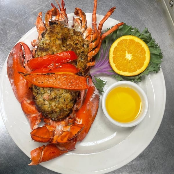 Stuffed lobster with roasted peppers, an orange slice, and melted butter on a white plate.