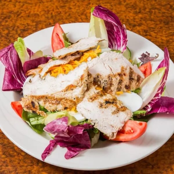 Grilled chicken salad with mixed greens, tomatoes, cheese, and hard-boiled egg on a white plate.