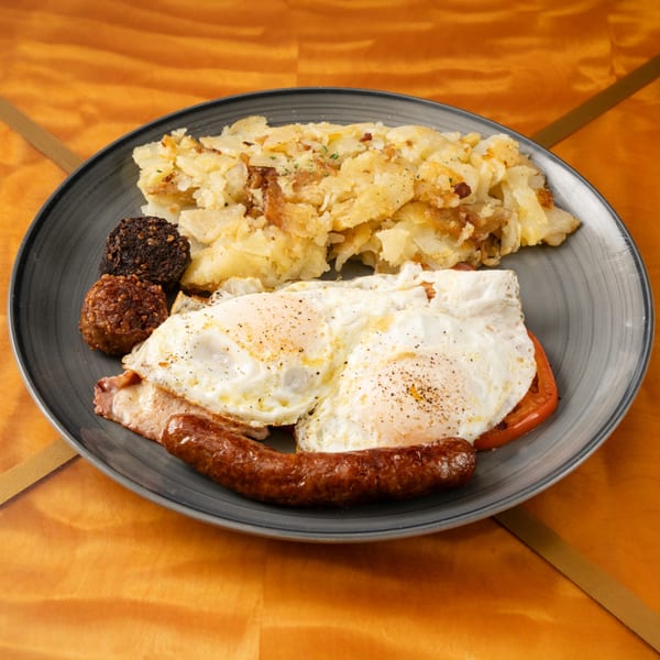 A diner breakfast plate with fried eggs, sausage, bacon, hash browns, and two dark patties.
