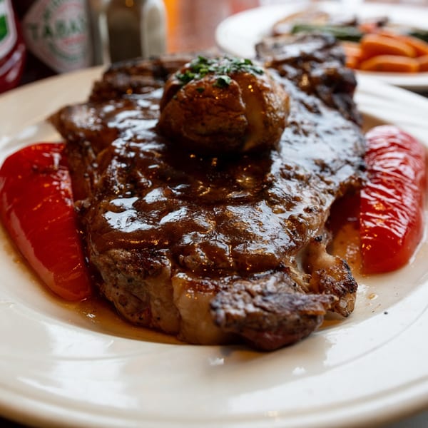 A juicy steak with gravy, a baked potato, and red bell peppers on a white plate.
