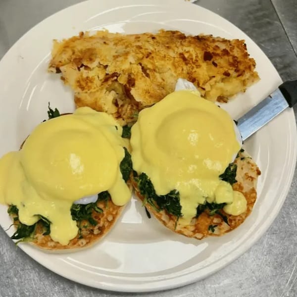 Eggs Benedict with spinach and hollandaise sauce, served with a side of hash browns.
