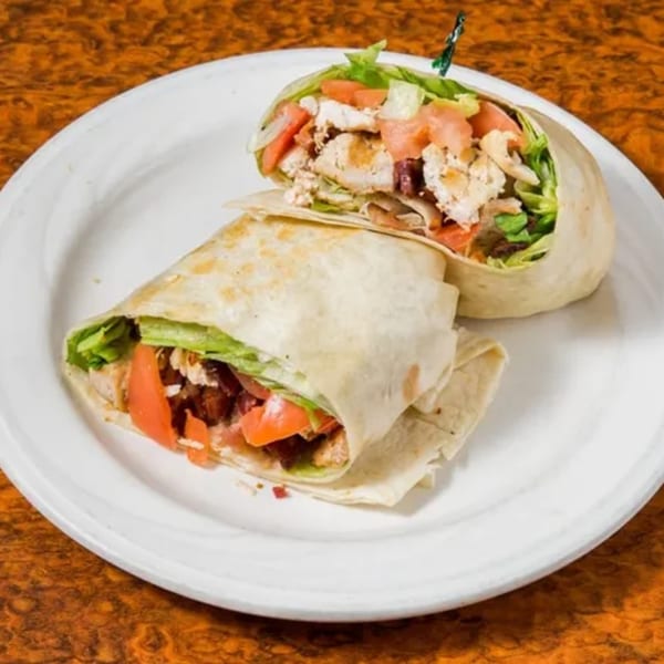Two halves of a chicken wrap with lettuce, tomatoes, and bacon on a white plate.