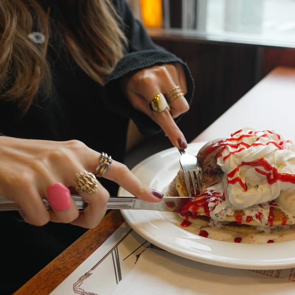 A person cuts into a stack of pancakes topped with whipped cream and strawberry syrup at Georgia Diner.