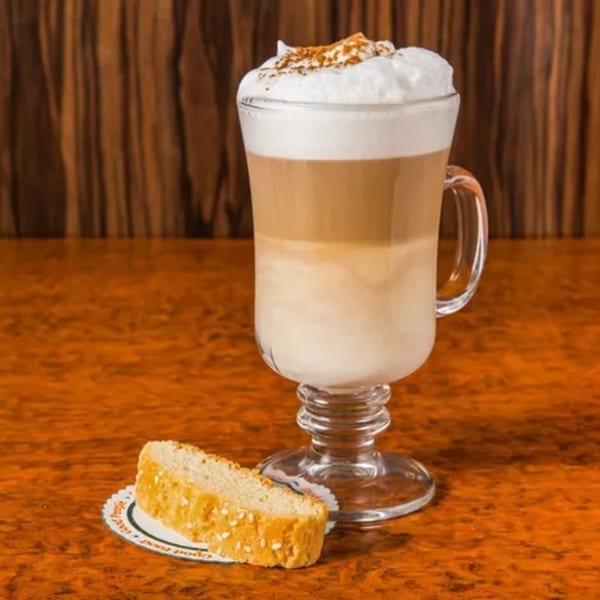 Layered latte with whipped cream and cinnamon, served with a biscotti on a diner counter.