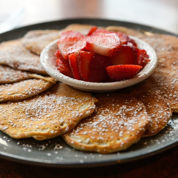 Golden pancakes dusted with powdered sugar, served with a side of fresh sliced strawberries.